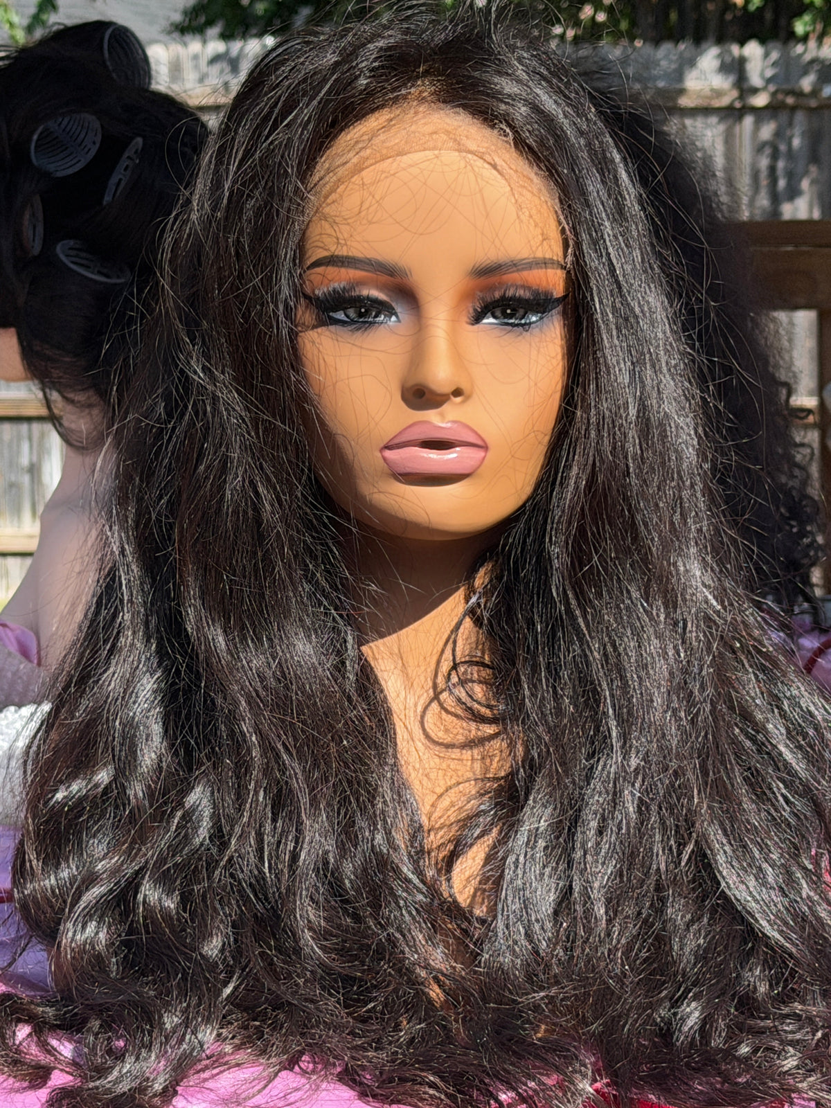 Long, wavy black wig with a lace front, displayed on a mannequin head outdoors.