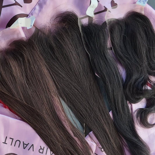 Three lengths of dark brown to black hair extensions laid out on pink branded hair clips and bags on a gray wooden surface.